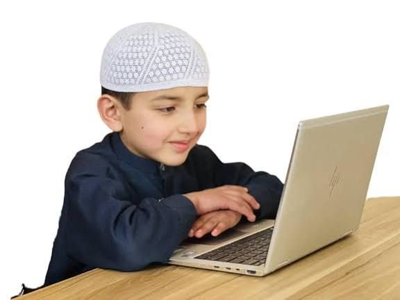 Smiling boy in kufi using a laptop for Quran class